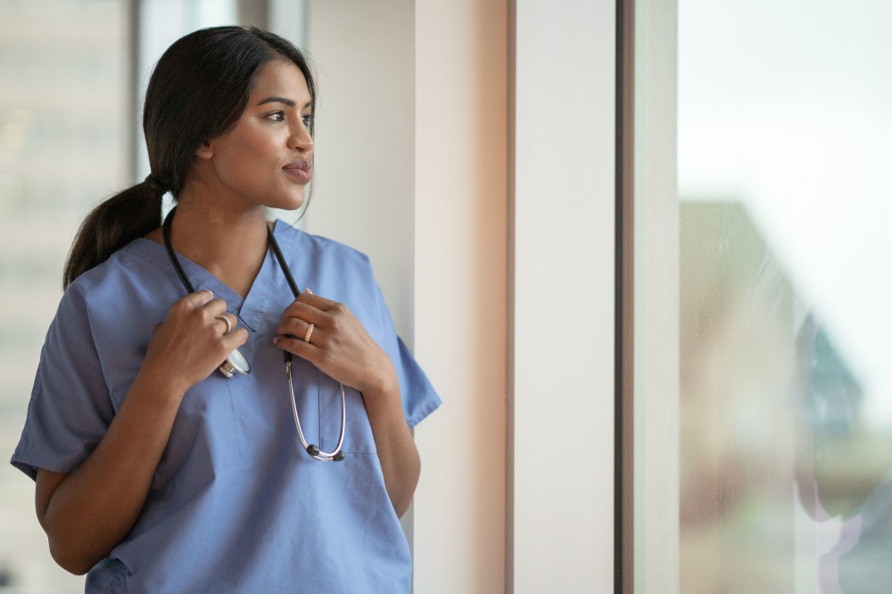 nursing student in scrubs and stethoscope looking out window