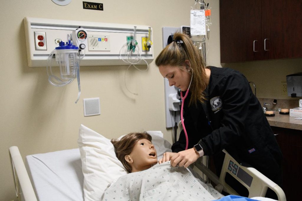 nursing student wearing stethoscope practicing on manikin