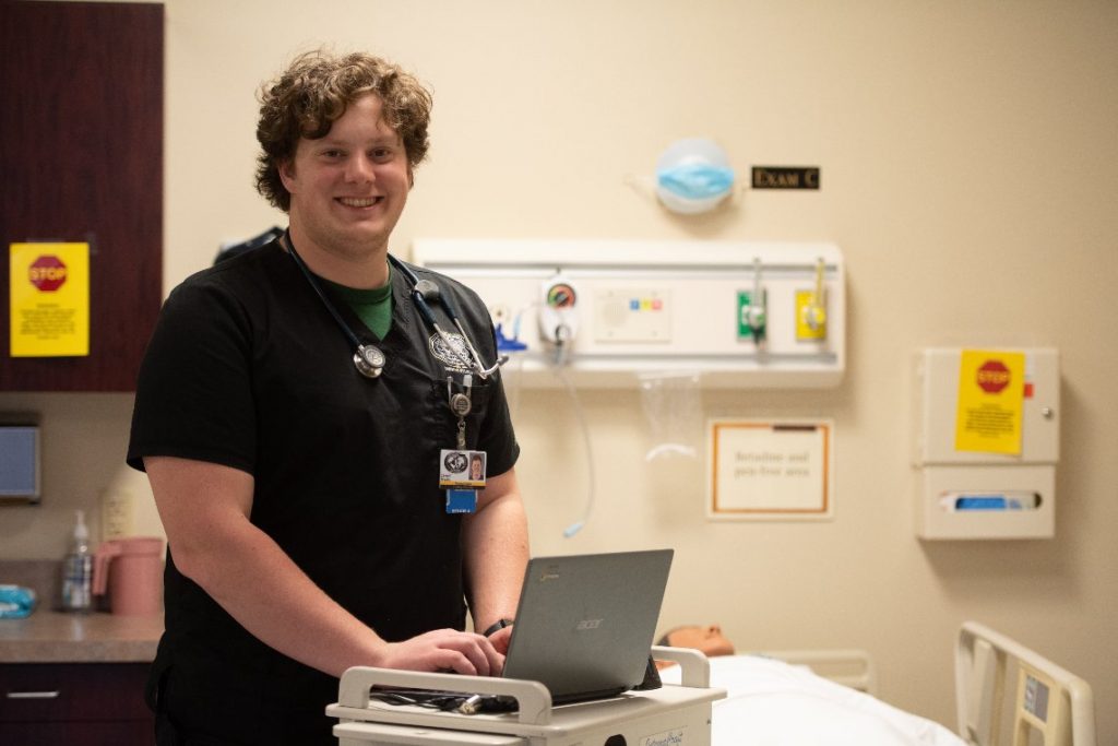 Harding ABSN student with computer and manikin in clinical setting