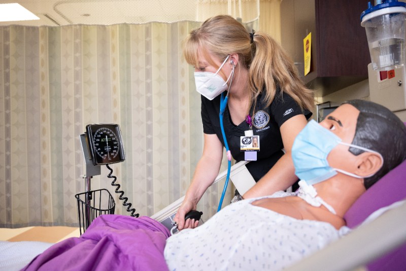 Harding ABSN student in scrubs practicing on manikin