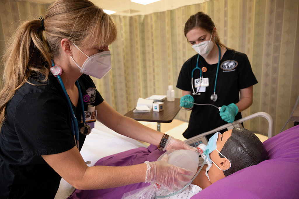 two nursing students standing over manikin administering oxygen