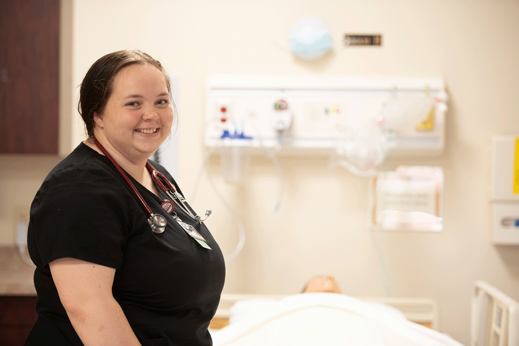 nursing student smiling while standing over manikin